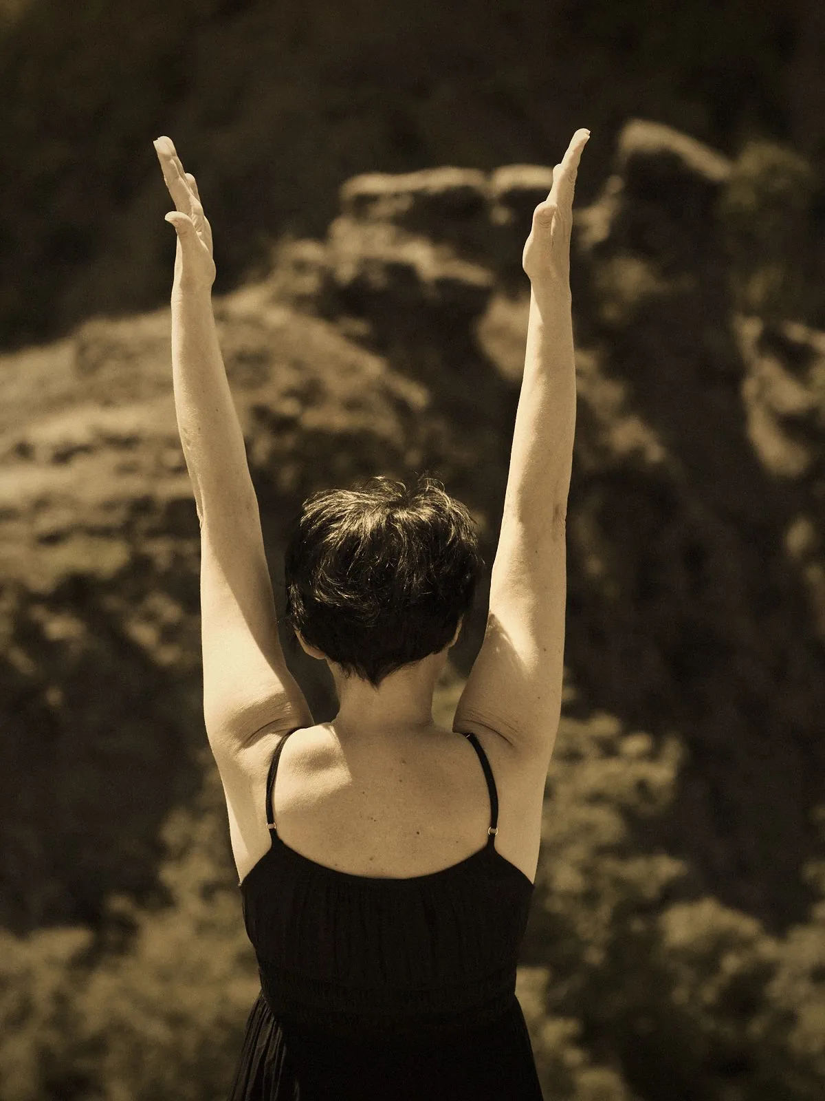 Yoga and meditation breathwork with arms raised overhead against dark rocks